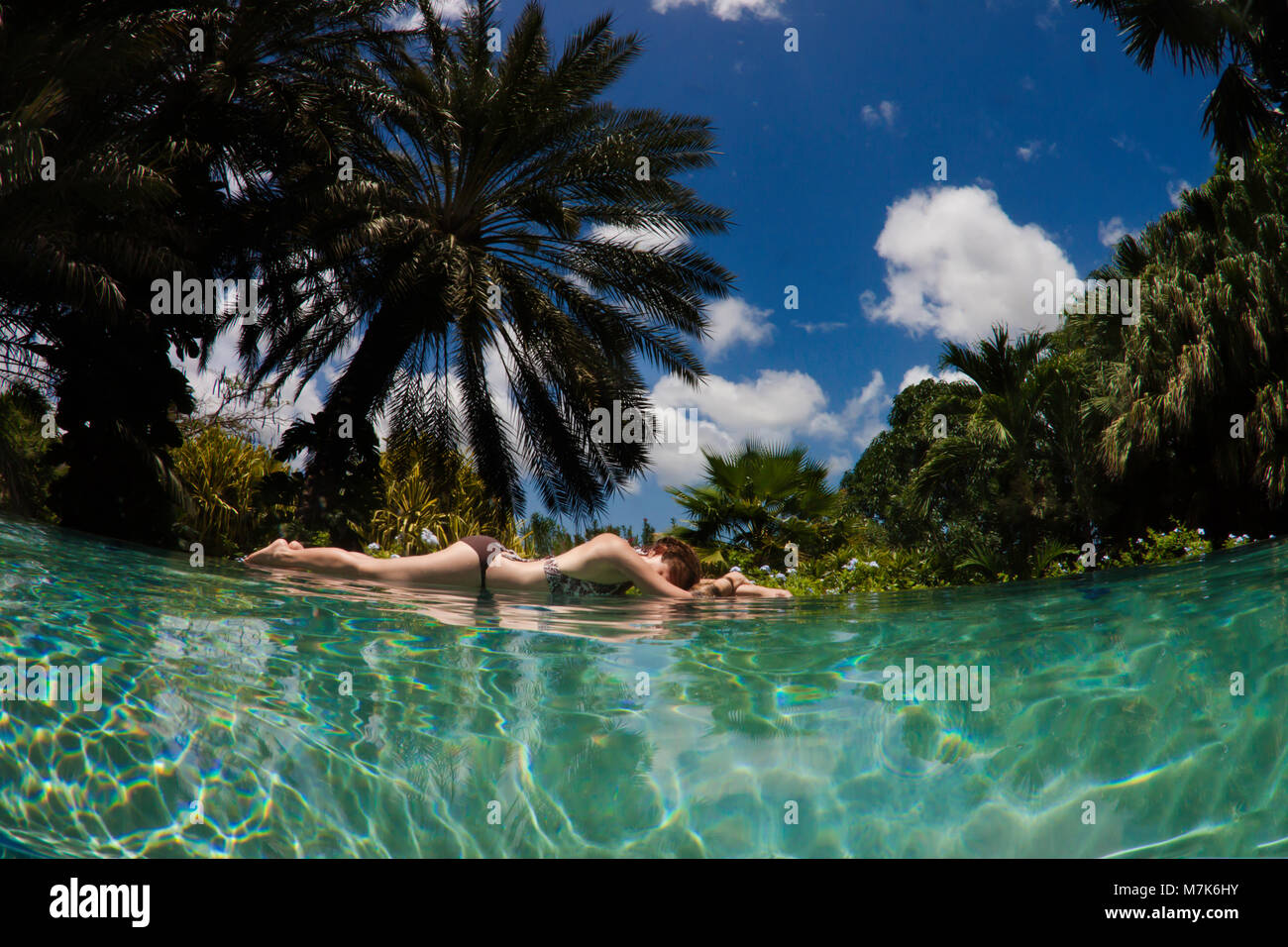 A woman lies at the edge of an infinity pool with a tropical background on the island of Curacao, Netherlands Antilles, in the Caribbean. Stock Photo