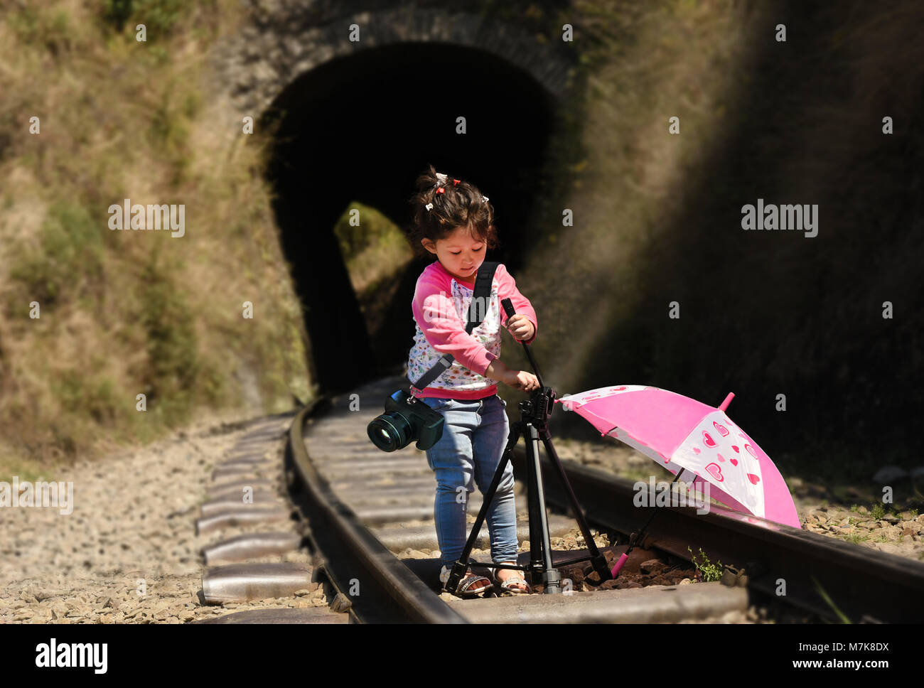 Little girl photographer with tripod and DSLR camera strapped on her shoulder. Stock Photo