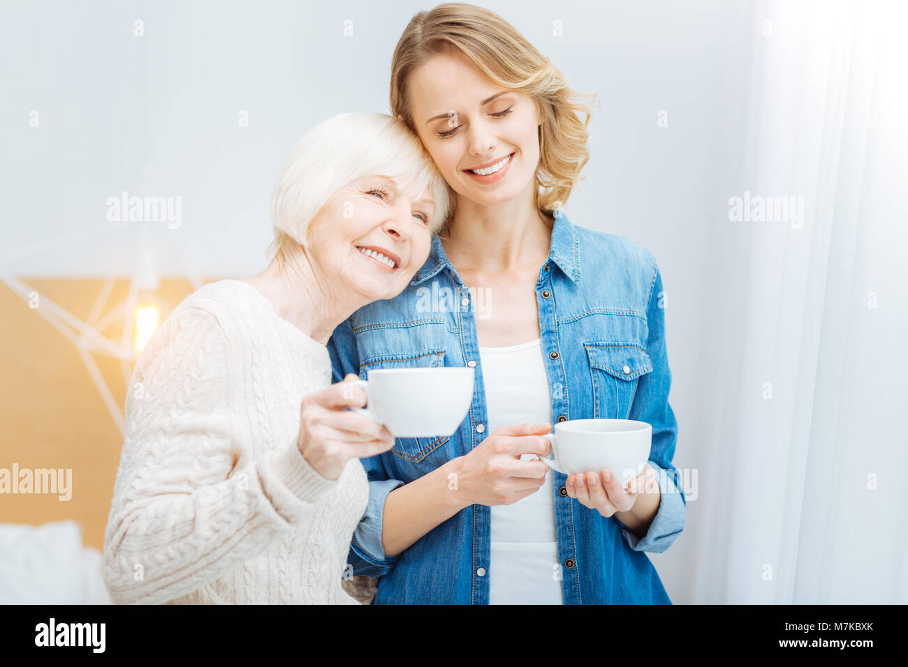 Cute young woman closing her eyes and smiling while being with grandmother Stock Photo