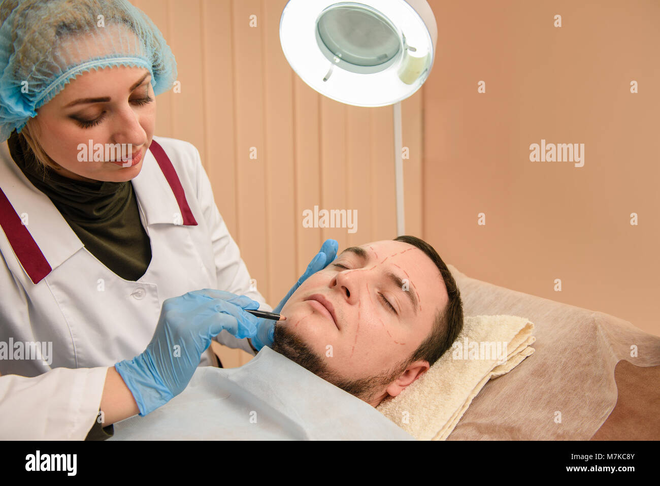 Man in plastic surgery clinic making operation plan. Doctor hands in rubber gloves make pencil contours on patient Stock Photo