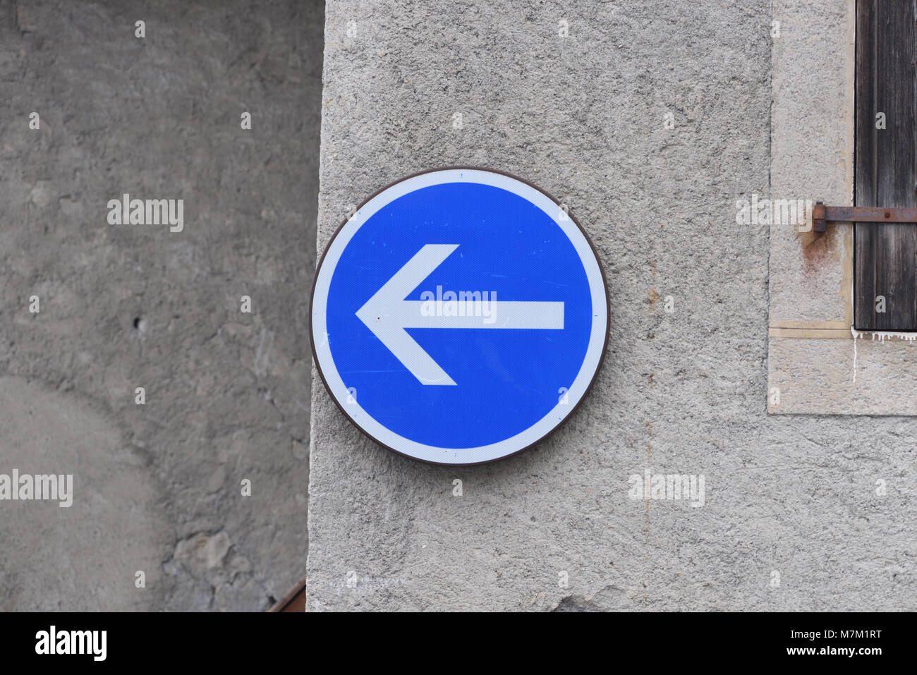 A blue and white traffic direction sign in the form of an arrow on a stone wall. Samoens, Haute Savoie, France. Stock Photo