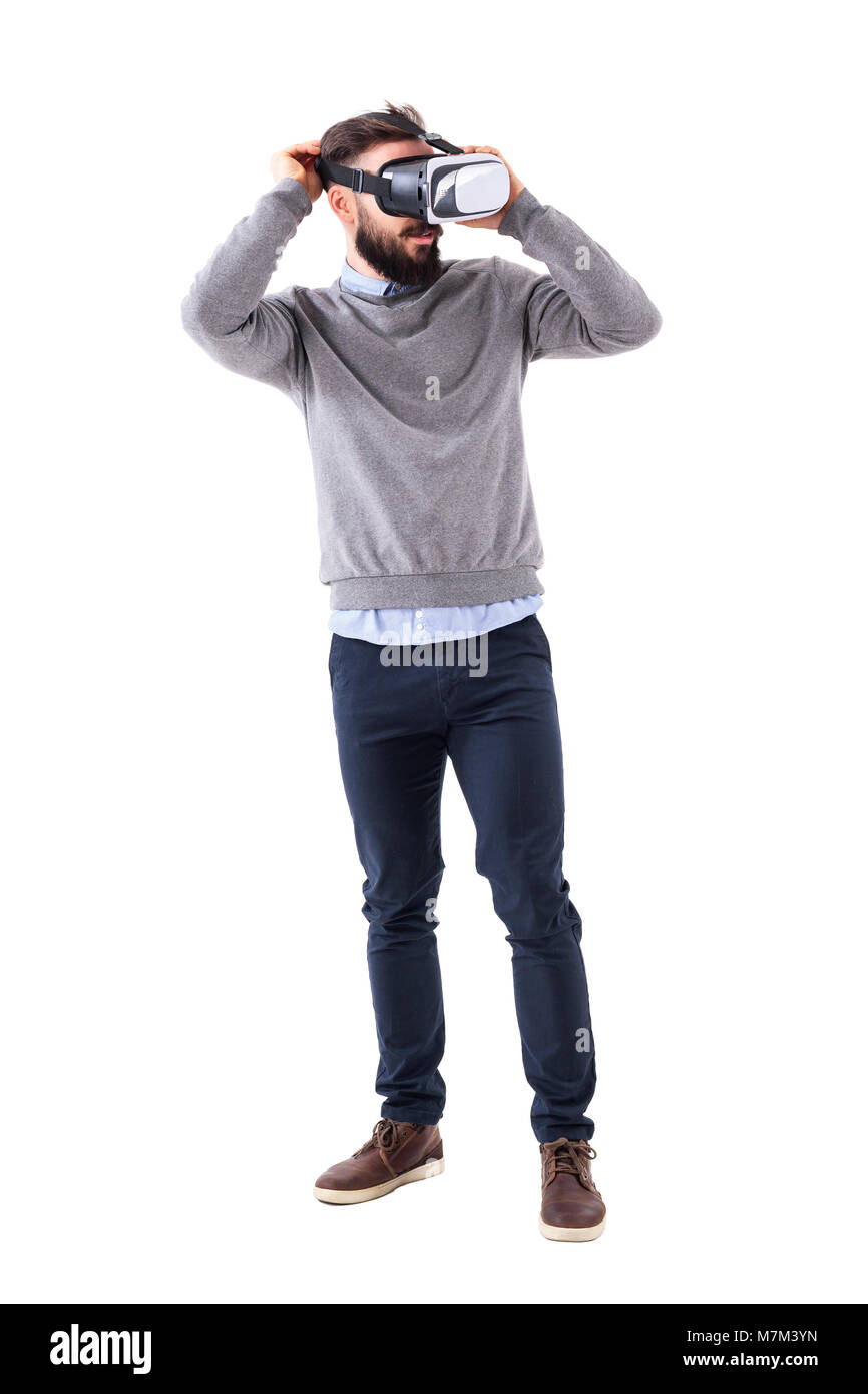 Young excited formal bearded man putting on vr glasses and looking away. Full body length portrait isolated on white studio background. Stock Photo