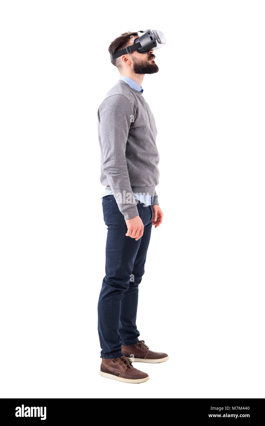 Side view of speechless young man having virtual reality glasses experience looking up above. Full body portrait isolated on white background. Stock Photo