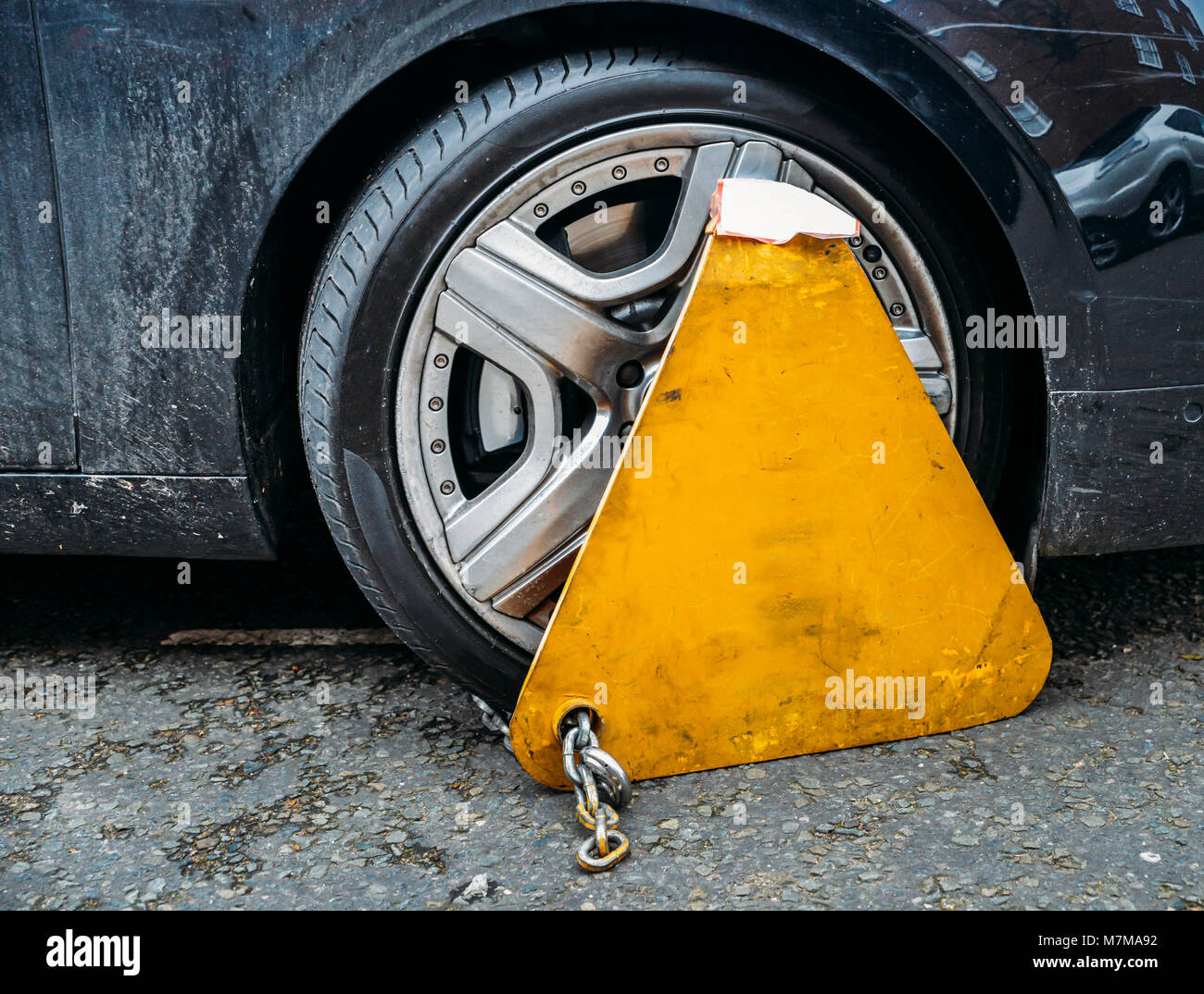 Yellow triangle wheel clamp locked with messing lock and chain on an illegally parked car Stock Photo