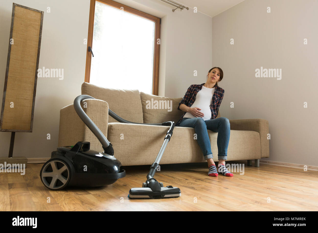 Pregnant woman sitting on couch tired of vacuuming. Household and
