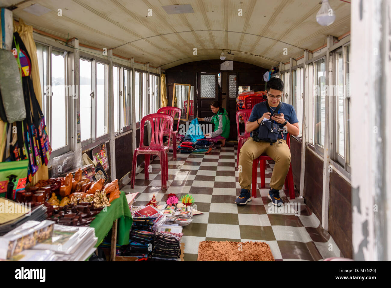 A tourist sits on a plastic chair inside one of the Dragon boats which can be hired by tourists sailing on the Perfume River, Hue, Vietnam.  The family live on the boat and use this area as a bedroom at night. Stock Photo