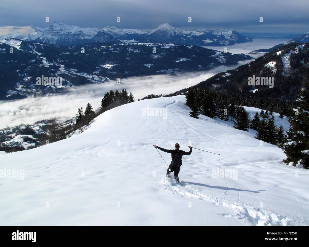 A woman snowshoes below La Bourgeoise overlooking the Giffre Valley and the town of Samoens in the French Alps Stock Photo