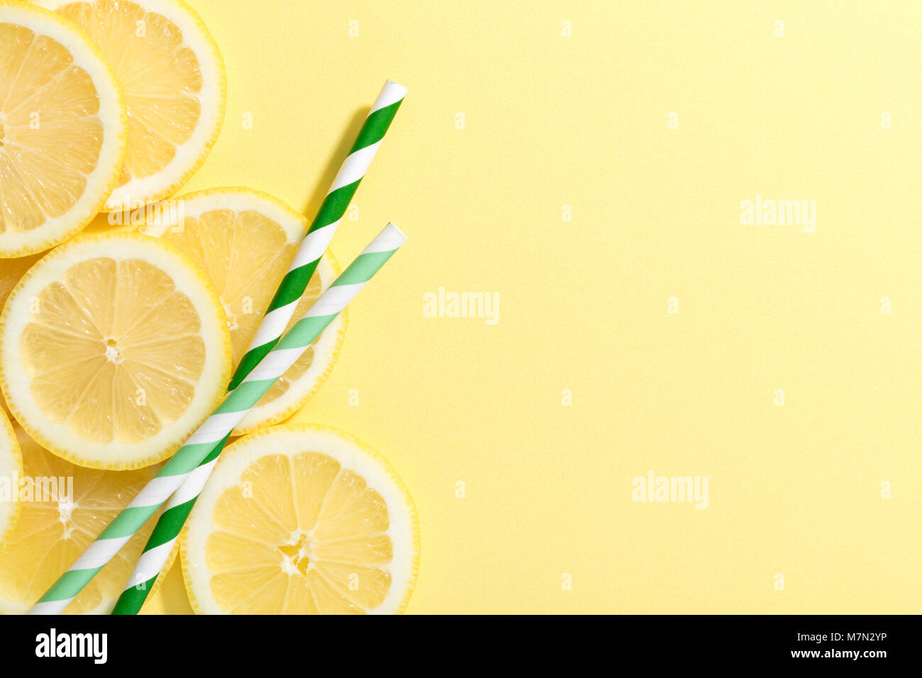 slices of lemon on yellow colored background with two straws green and white stripped Stock Photo