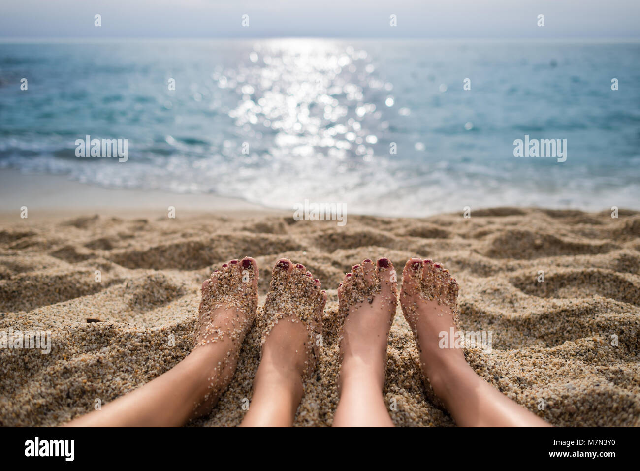Travel concept. Scenic view from beach on sea and sky. Two girls are sunbathing on sand. Close-up view on pair of human legs. Focus on beach and legs Stock Photo