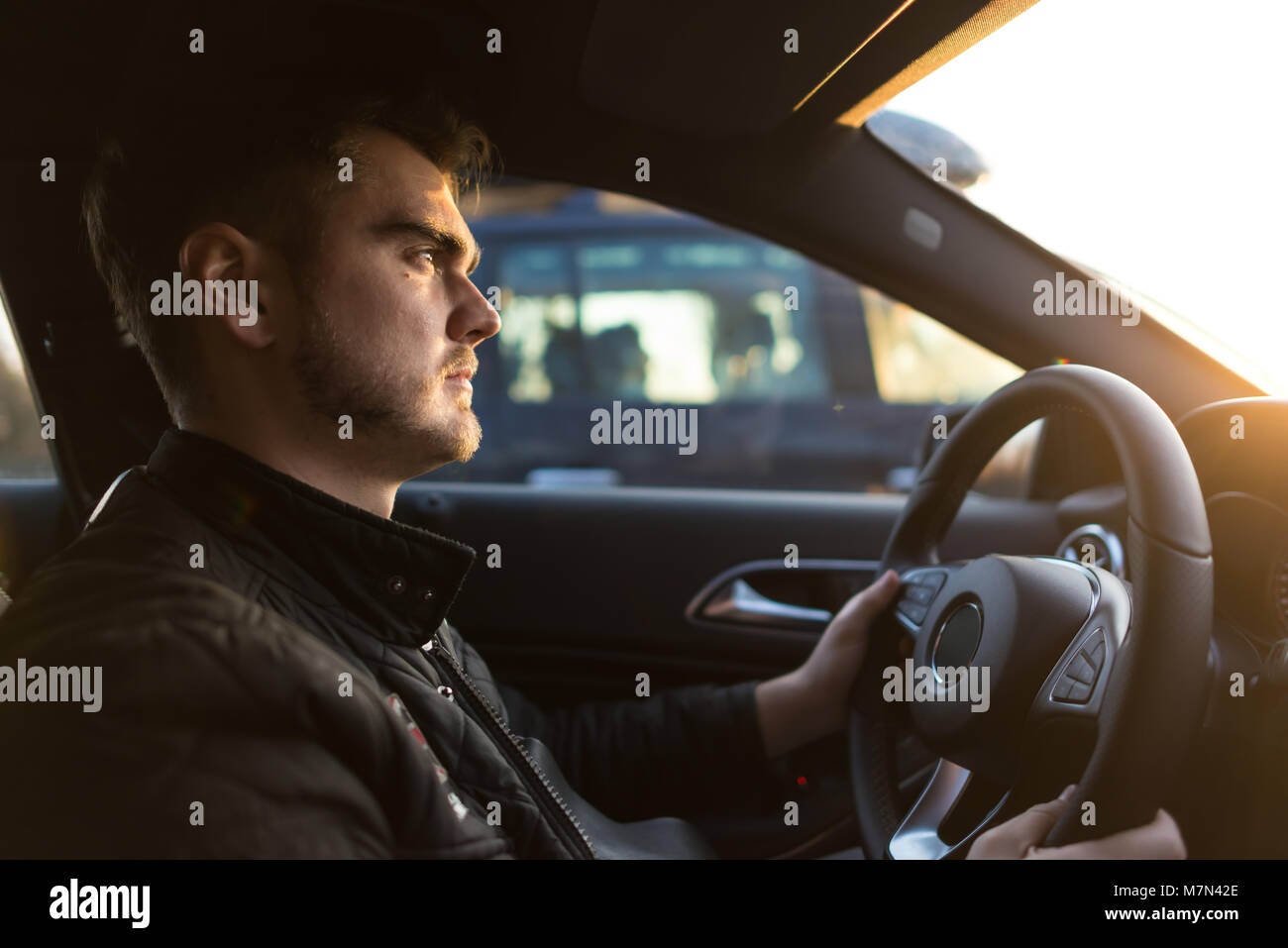Concentrated young man driving luxury car. Serious guy looking forward and holds hands on wheel. Successful man in hurry on business. Side view Stock Photo