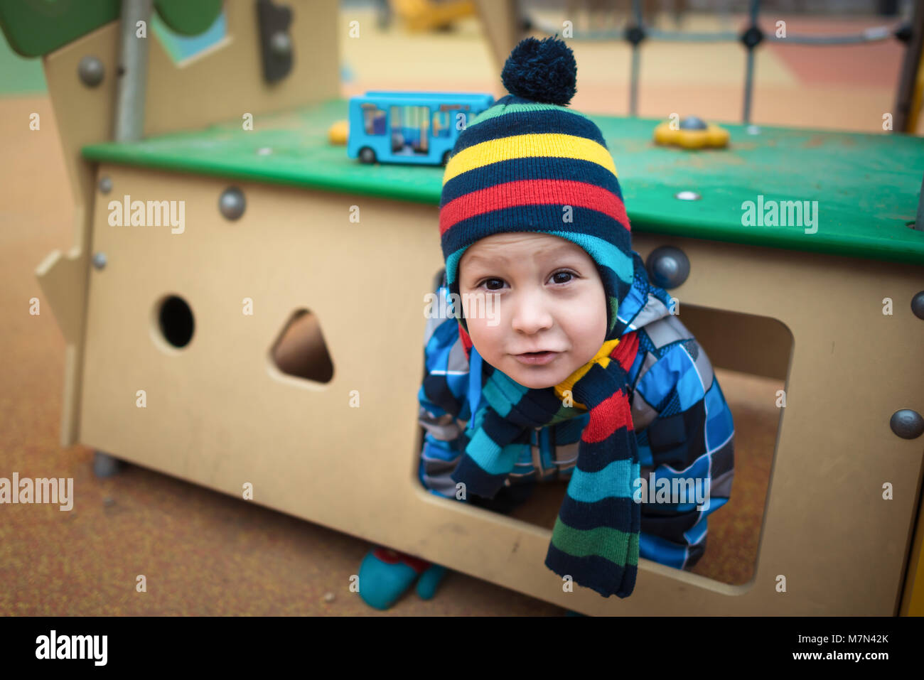 Beautiful child sits in small house at the playground area. Serious little boy playing in the yard and crawls out from hideaway Stock Photo
