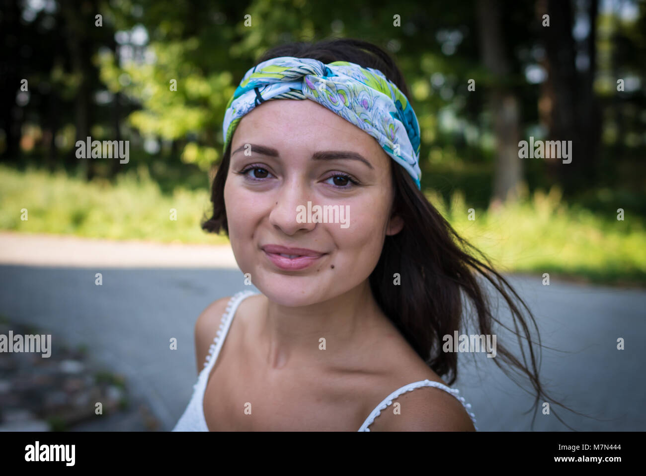 Portrait of young woman with colorful bandage on the head. Beautiful smiling girl is standing on the background of nature and trees Stock Photo