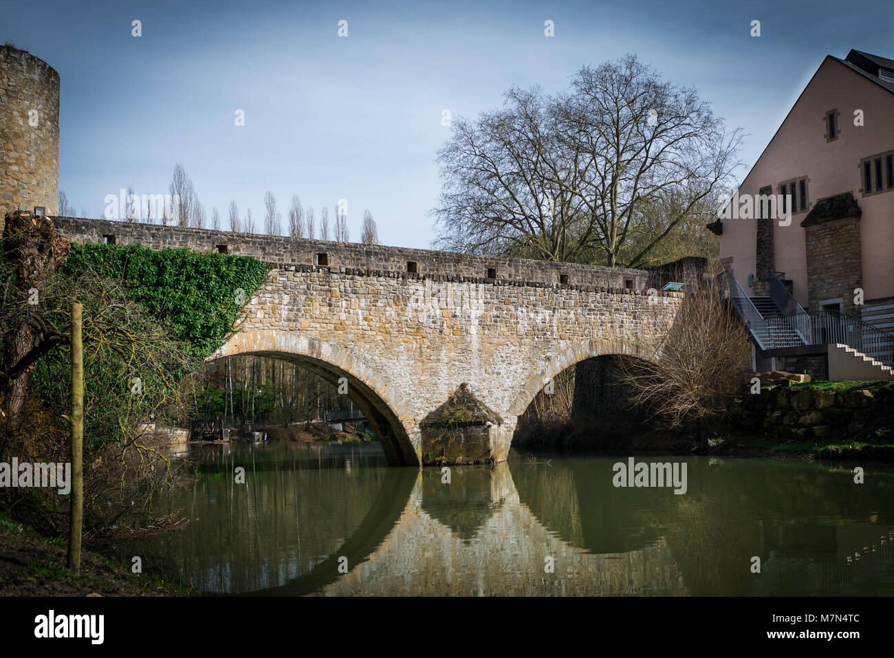 Beautiful antique bridge with on top over the river at old town. Reflections on the water. Authentic architecture in lower city in Luxembourg Stock Photo