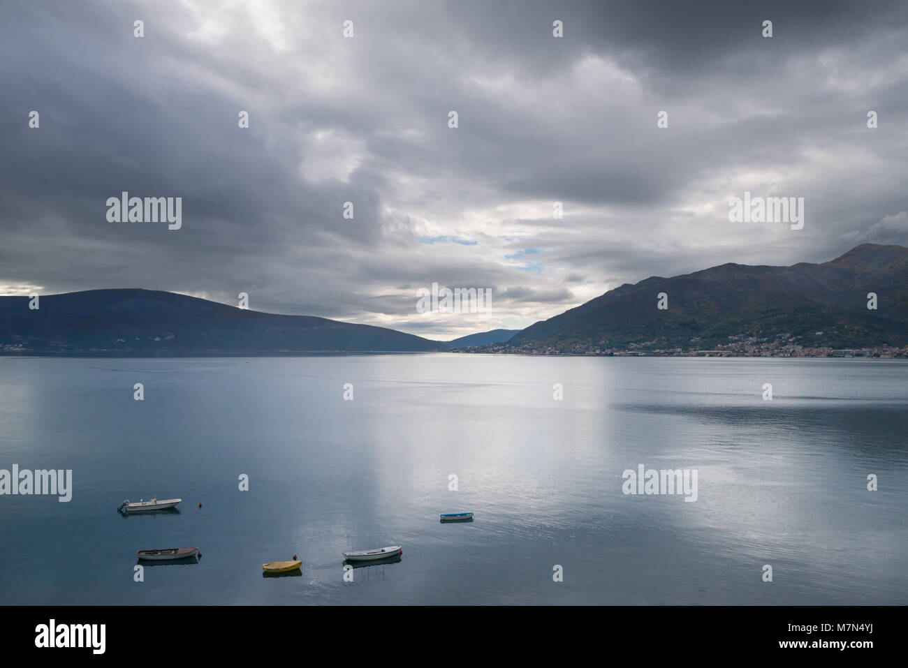 Landscape with small boats on the calm water. Dramatic clouds and mountains on background in the bay in Montenegro. Stock Photo