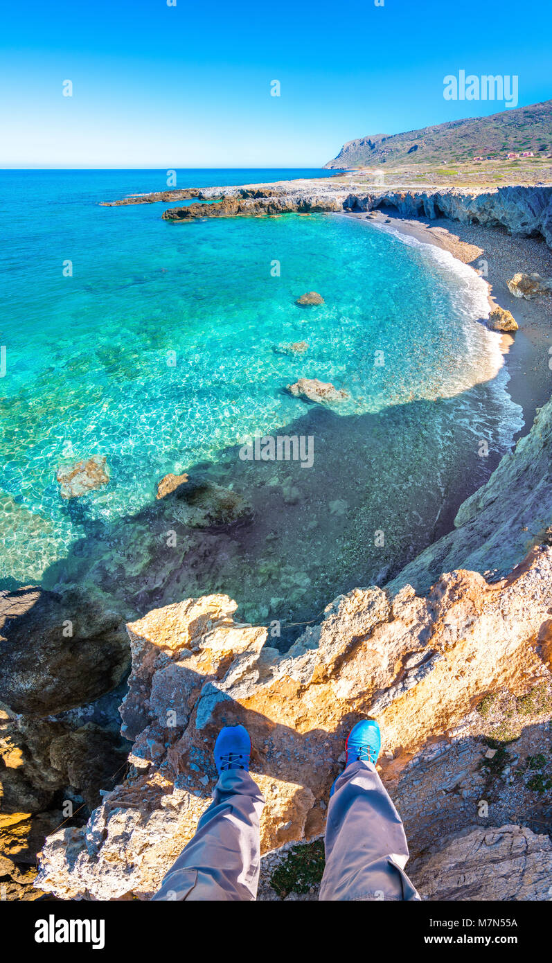 Vertorama of a man standing on the edge of the cliff above a beautiful beach in Milatos, Crete, Greece. Stock Photo