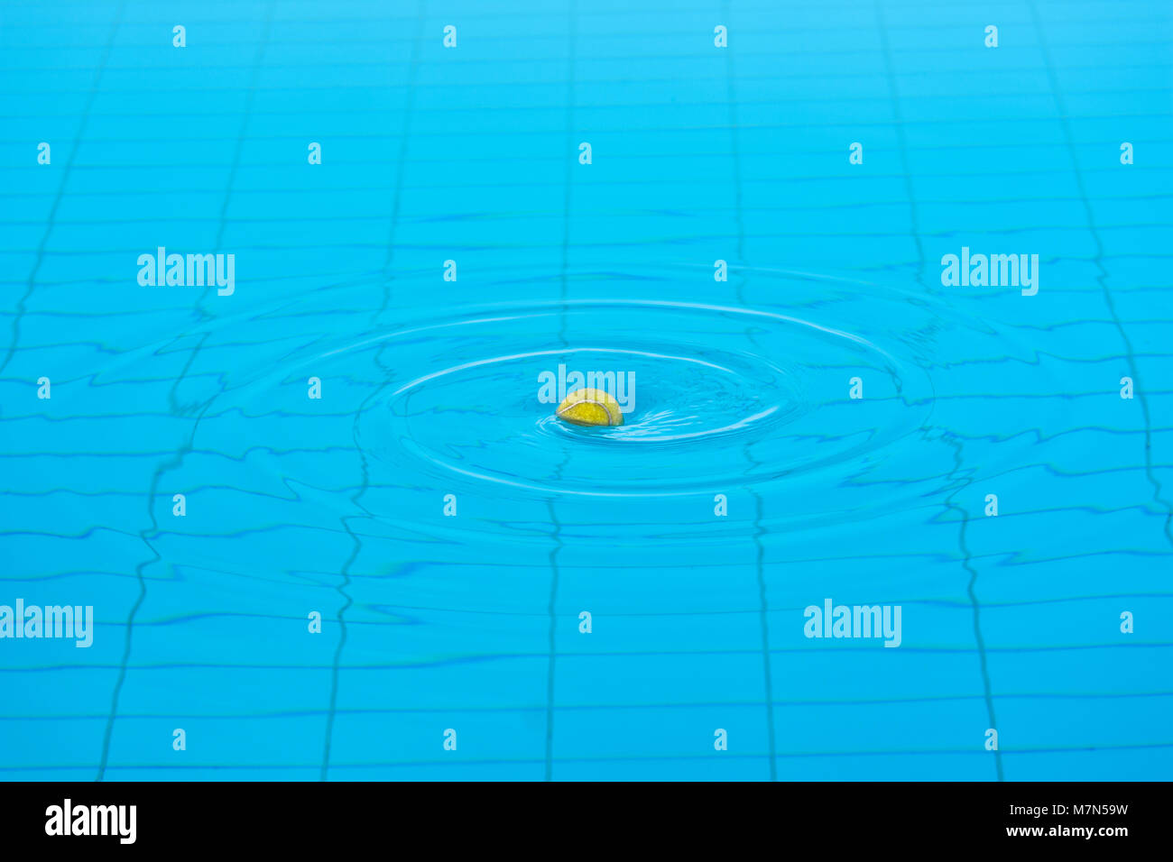 Tennis ball in the center of twirling water surface of a swimming pool. Stock Photo