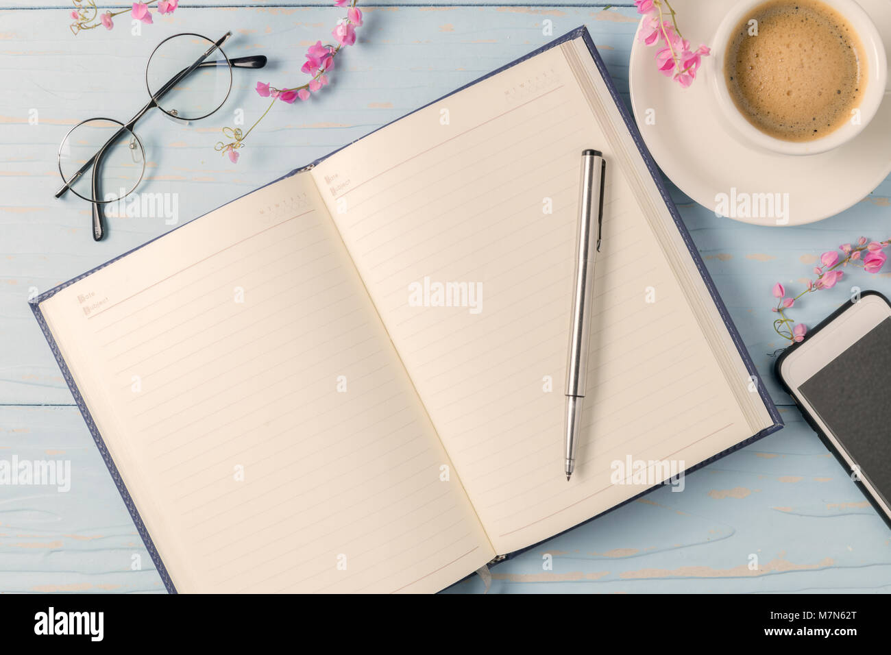 pen on blank diary book with hot black coffee and glasses on old blue wood background, vintage tone Stock Photo