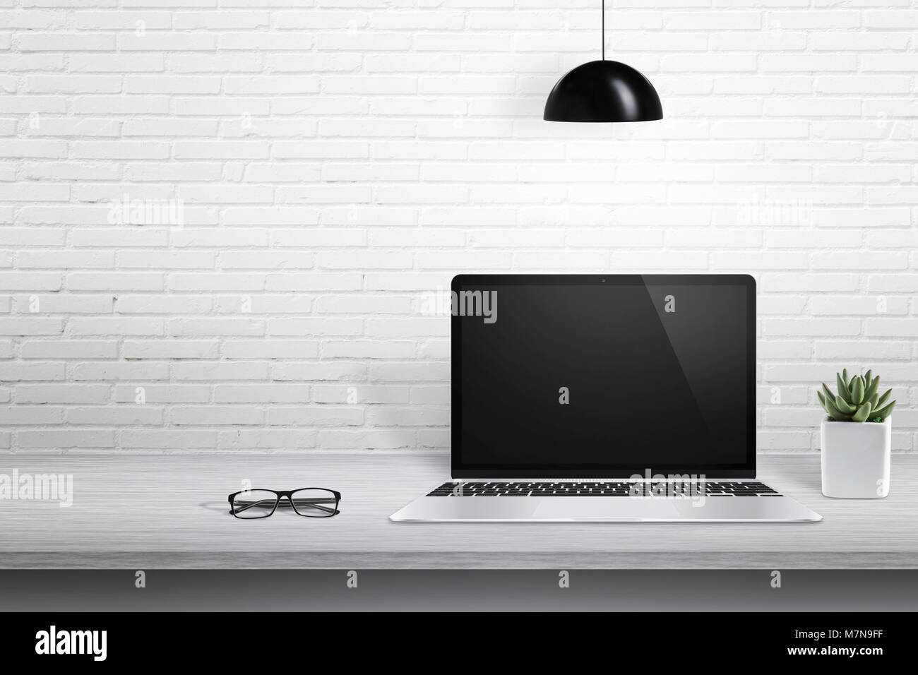 Modern laptop computer on desk with blank screen for mockup. White brick wall in background with free space for text. Stock Photo