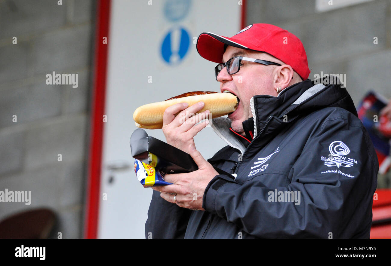 Football fan eating a large hotdog sausage bap roll at The Sky Bet League 2 match between Crawley Town and Morecambe at the Checkatrade Stadium in Crawley. 10 Mar 2018 - Editorial use only. No merchandising. For Football images FA and Premier League restrictions apply inc. no internet/mobile usage without FAPL license - for details contact Football Dataco Stock Photo