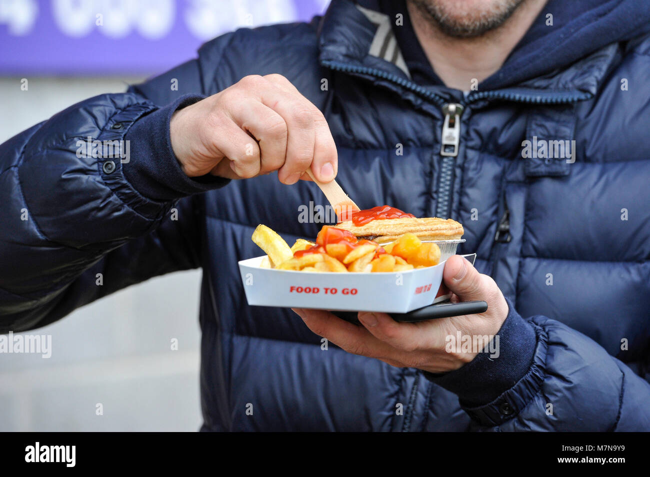 Football fan with Pie and chips with tomato sauce fast food takeaway food - Editorial use only. No merchandising. For Football images FA and Premier League restrictions apply inc. no internet/mobile usage without FAPL license - for details contact Football Dataco Stock Photo