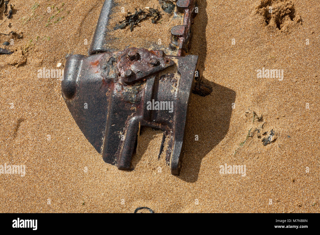A large metal object rusting on the beach, half buried in sand ...
