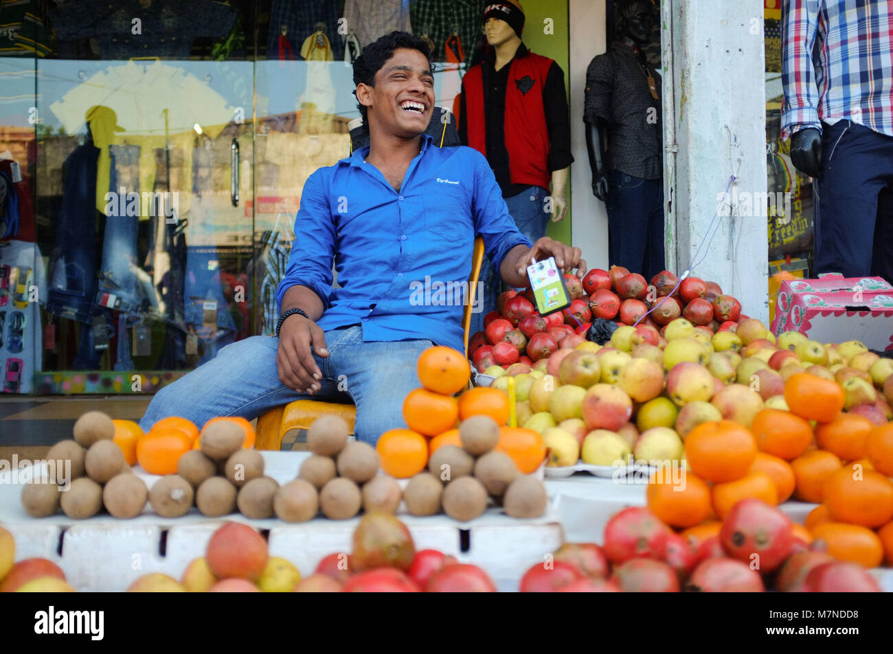 GOA, INDIA - JANUARY 27, 2015: Street fruit vendor sitting and laughing at fruit stand. Stock Photo