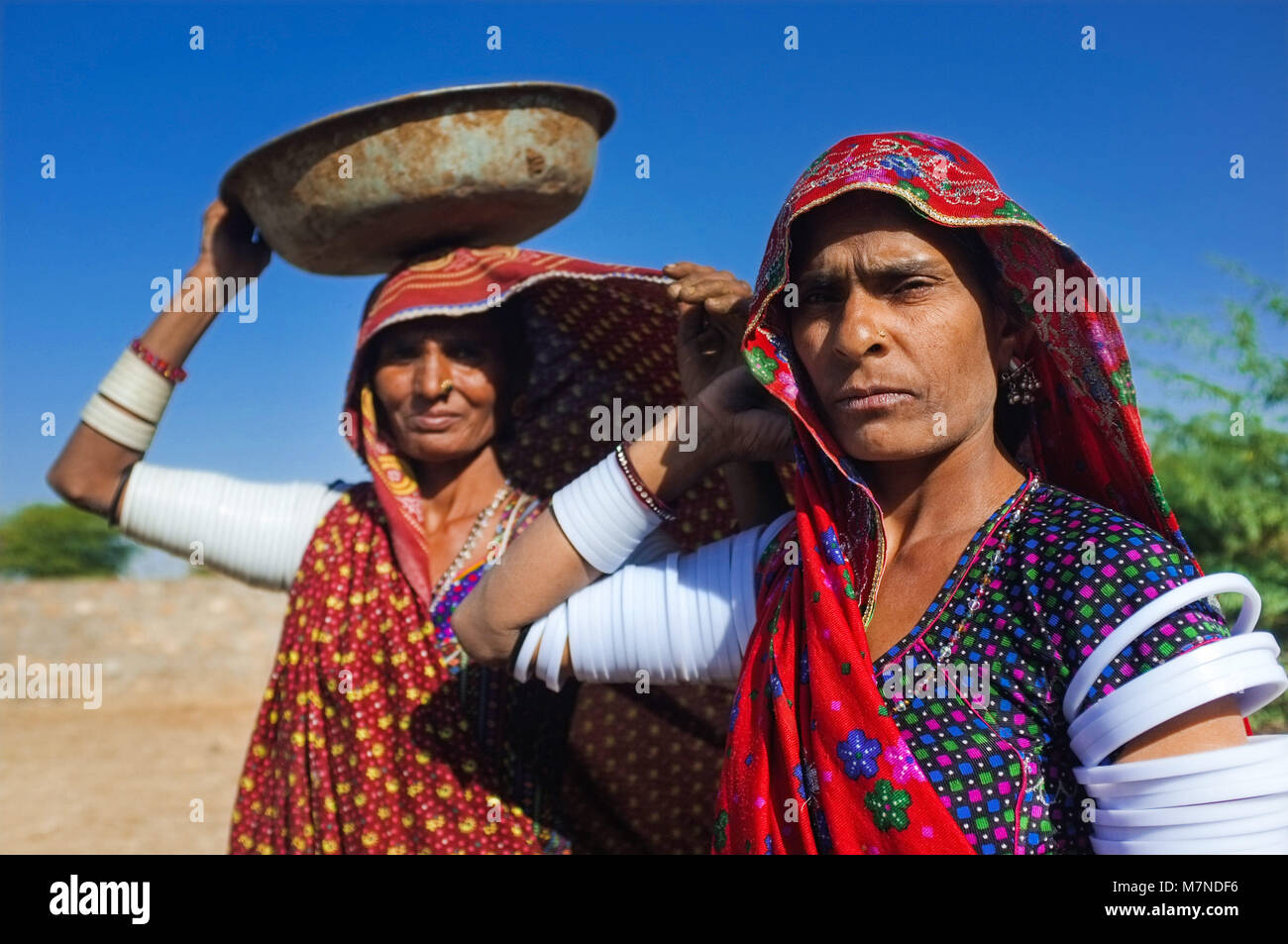 GODWAR REGION, INDIA - 14 FEBRUARY 2015: Rabari tribeswomen stand in field wearing sarees and upper-arm bracelets. One balances bucket on head. Rabari Stock Photo