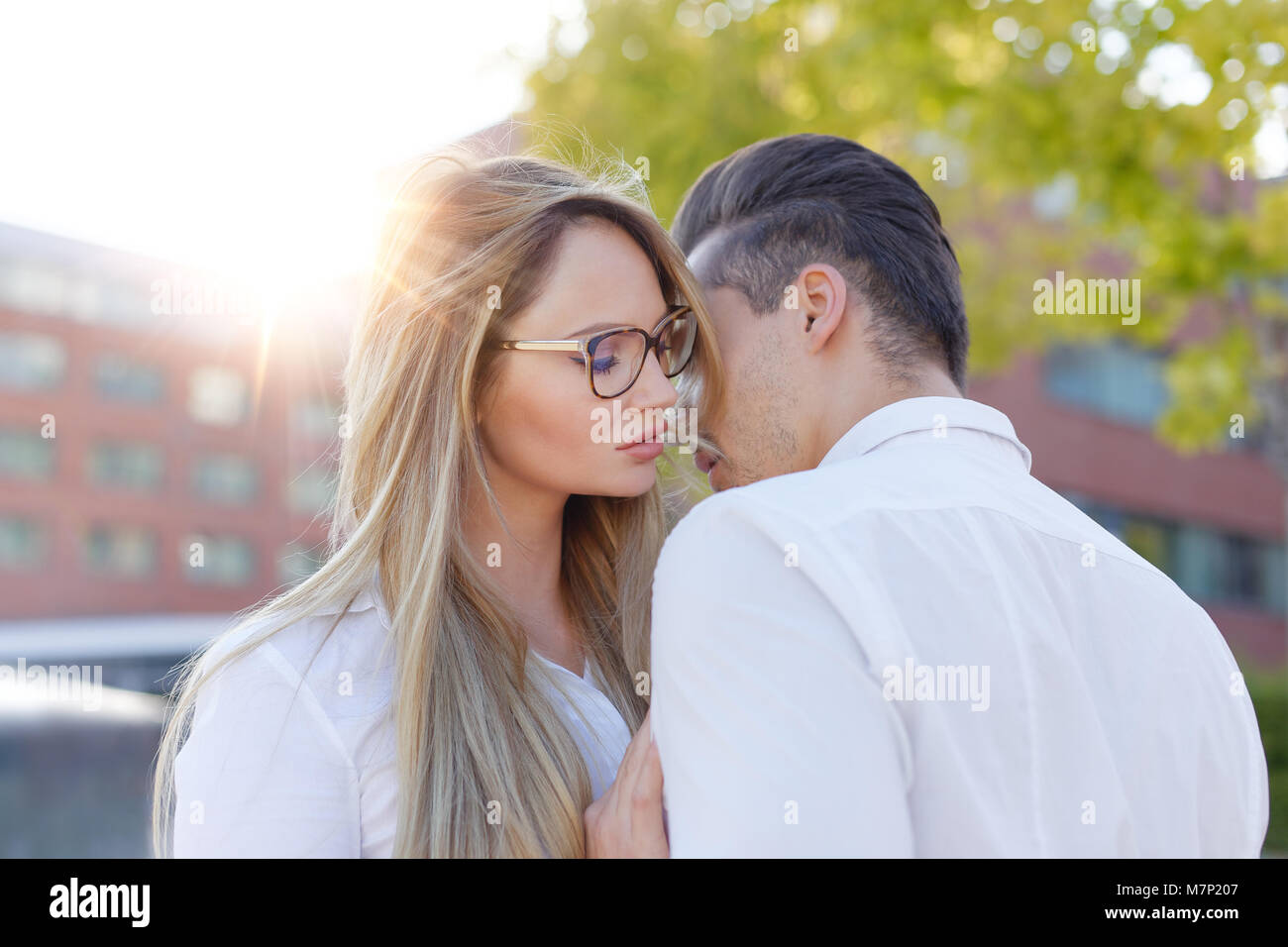 Young blonde woman whispers to man love outdoors in city, declaration of love Stock Photo