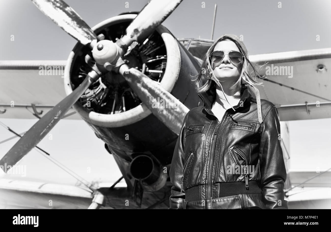 Beautiful girl in black jacket standing next a war aircraft. Retro