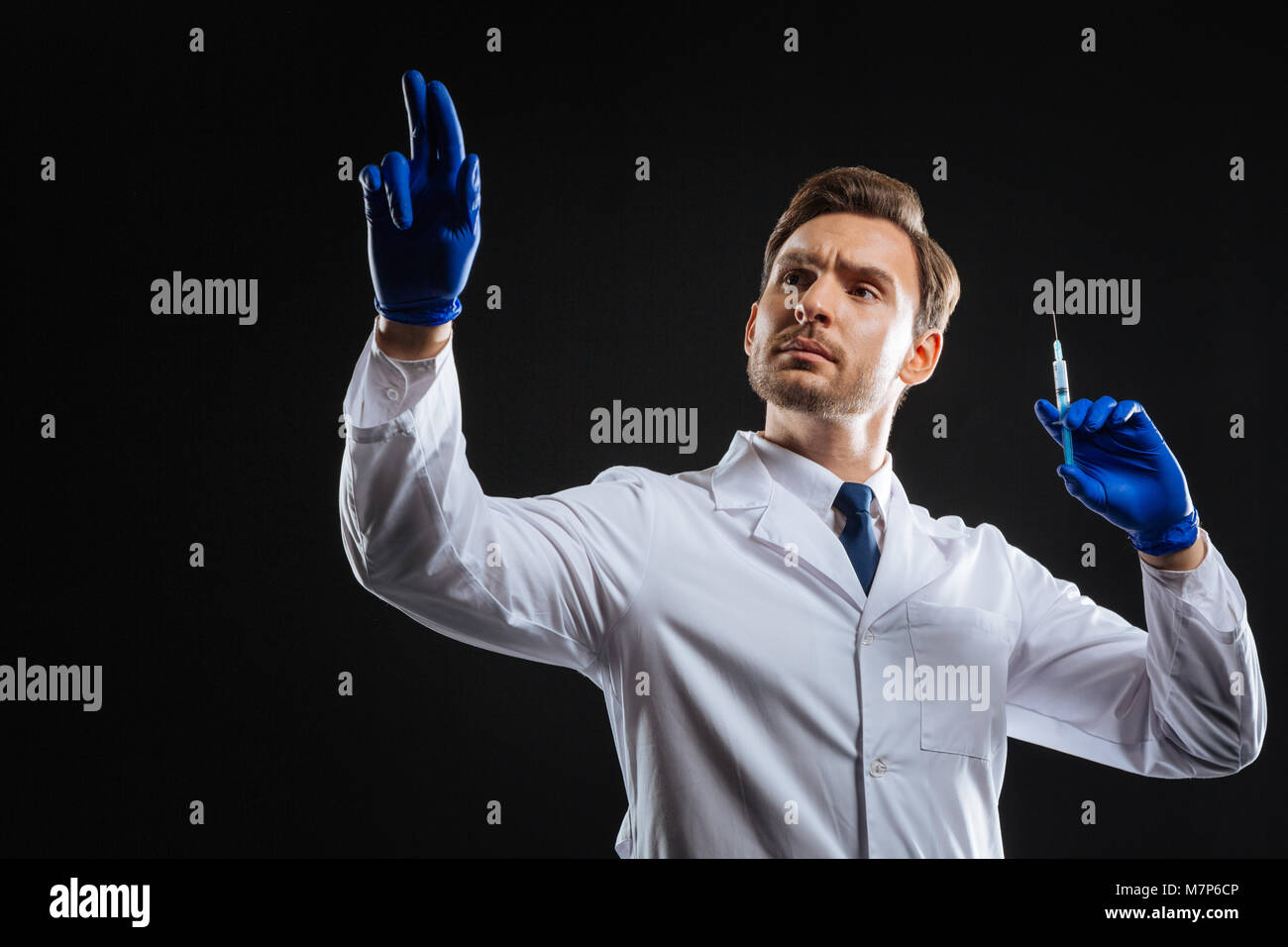 Responsible attentive medic holding a syringe lifting his hand. Stock Photo