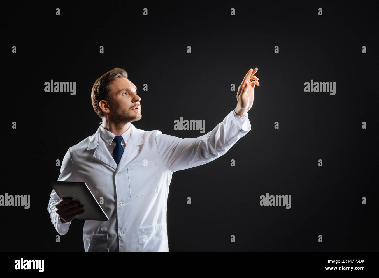 Smart concentrated medic standing and holding hand up. Stock Photo