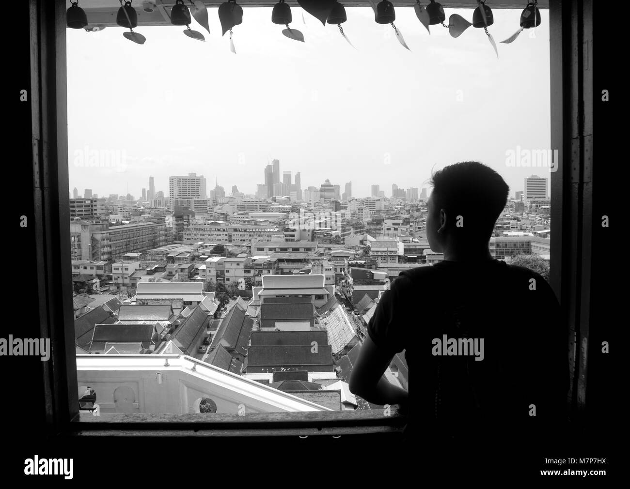 A young guy looking out of a window onto the Bangkok skyline, Thailand Stock Photo