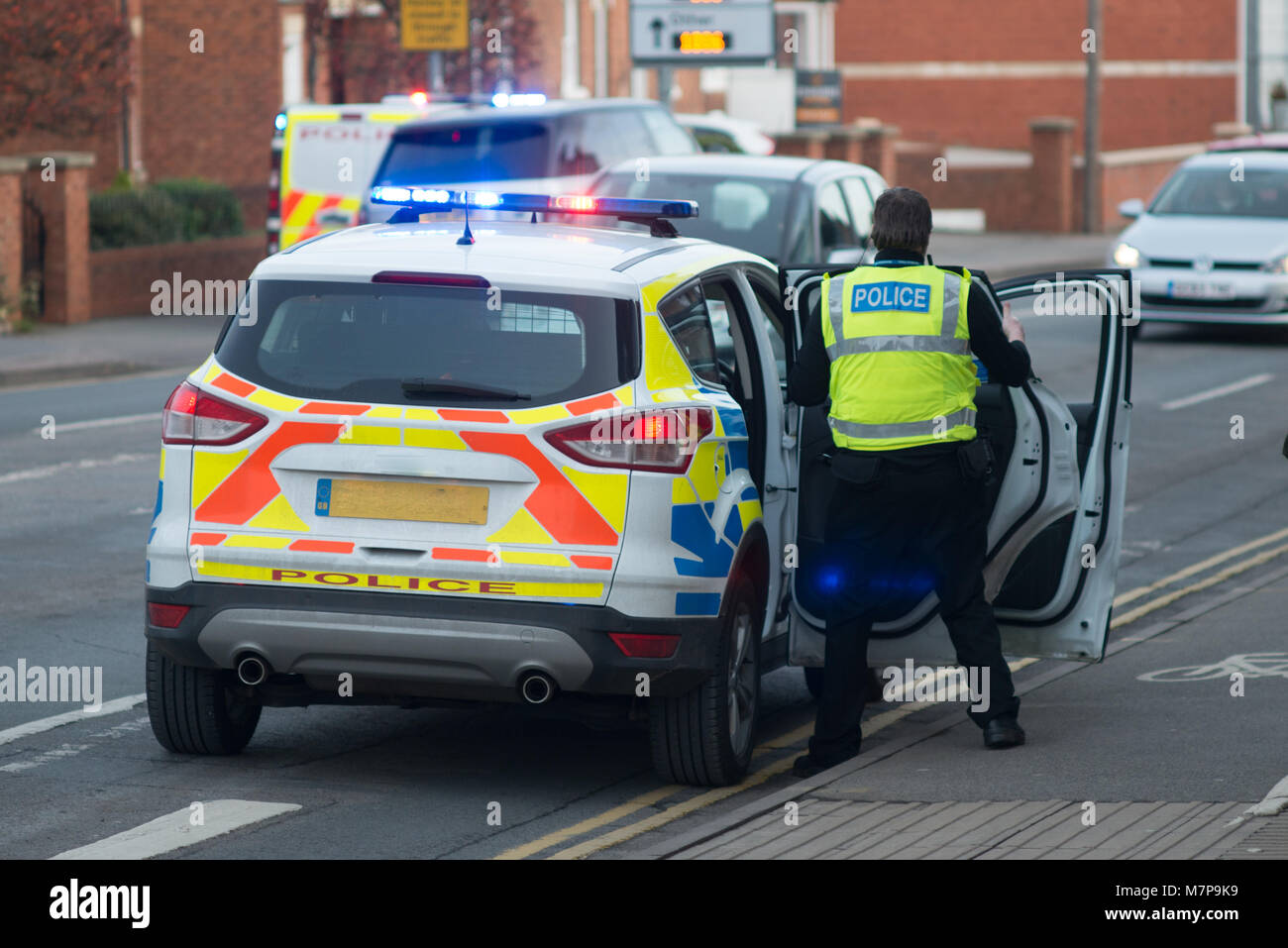 policeman enters vehicle with blue lights flashing and police riot van