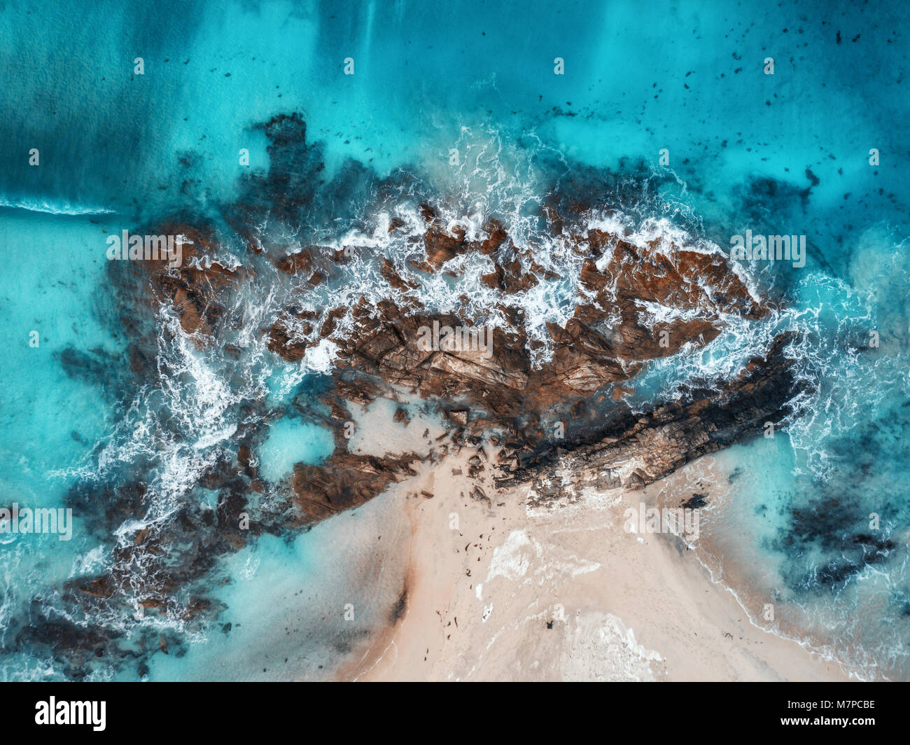 Aerial view of waves, rocks and transparent sea. Summer seascape with ocean, sandy beach, beautiful waves, cliffs, blue water at sunset. Top view from Stock Photo