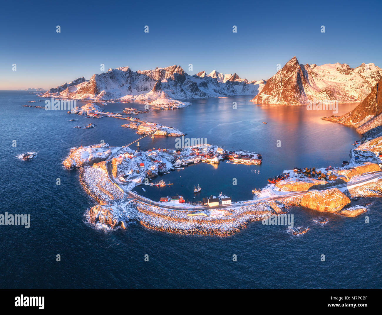 Aerial view of Reine and Hamnoy at sunset in winter. Amazing Lofoten islands, Norway. Panoramic landscape with blue sea, snowy mountains, rocks, villa Stock Photo
