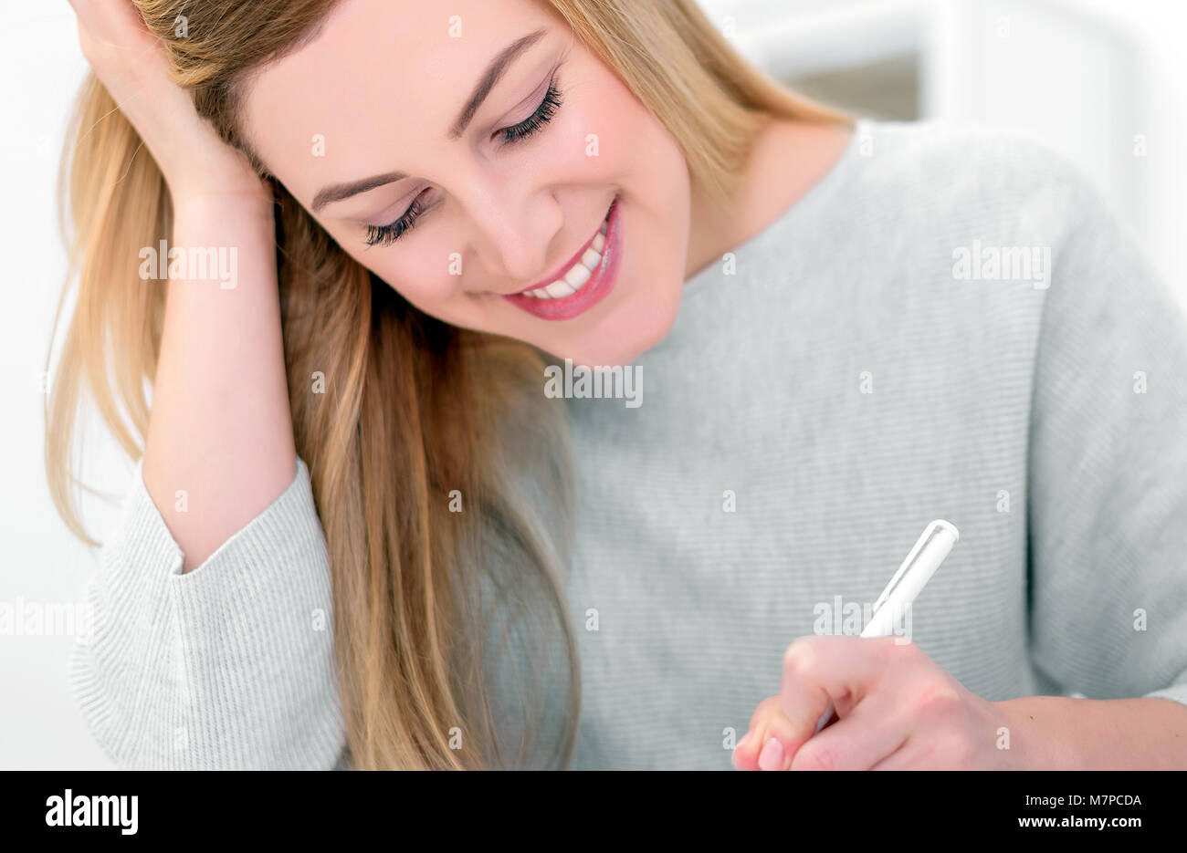 An attractive young woman in a good mood works with documents in the office or at home. Writes, fills papers at the desk with a laptop. Stock Photo