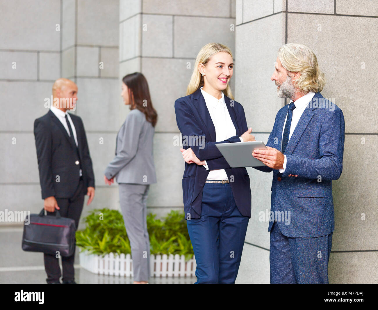 caucasian corporate executives standing discussing business using digital tablet in modern building. Stock Photo