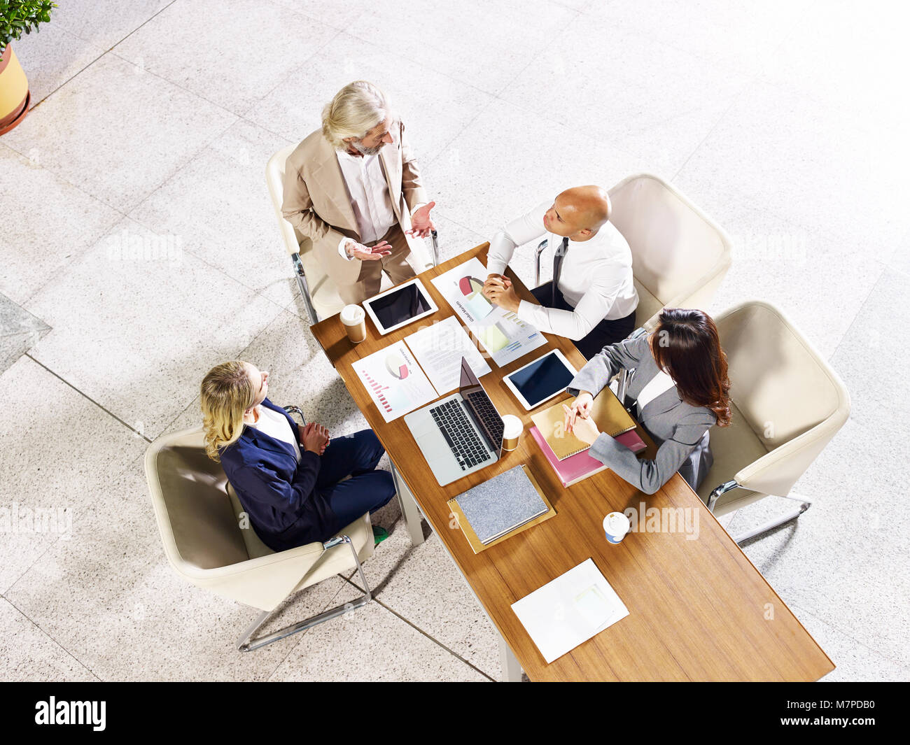 four multi-ethnic coporate business people meeting in modern office building, high angle view. Stock Photo