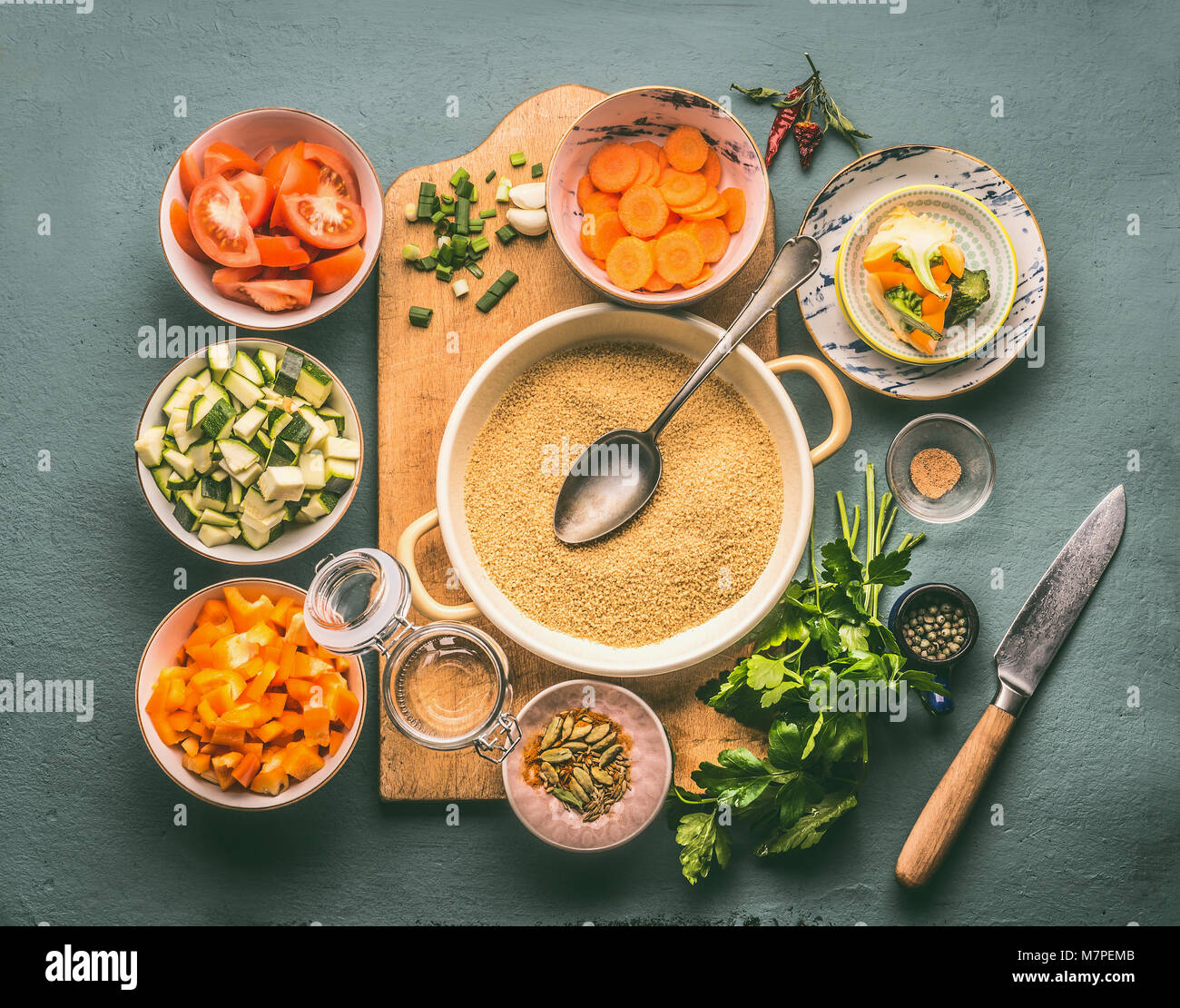 Couscous and vegetarian cooking ingredients in bowls on cutting board with spoon , gray background, top view Stock Photo