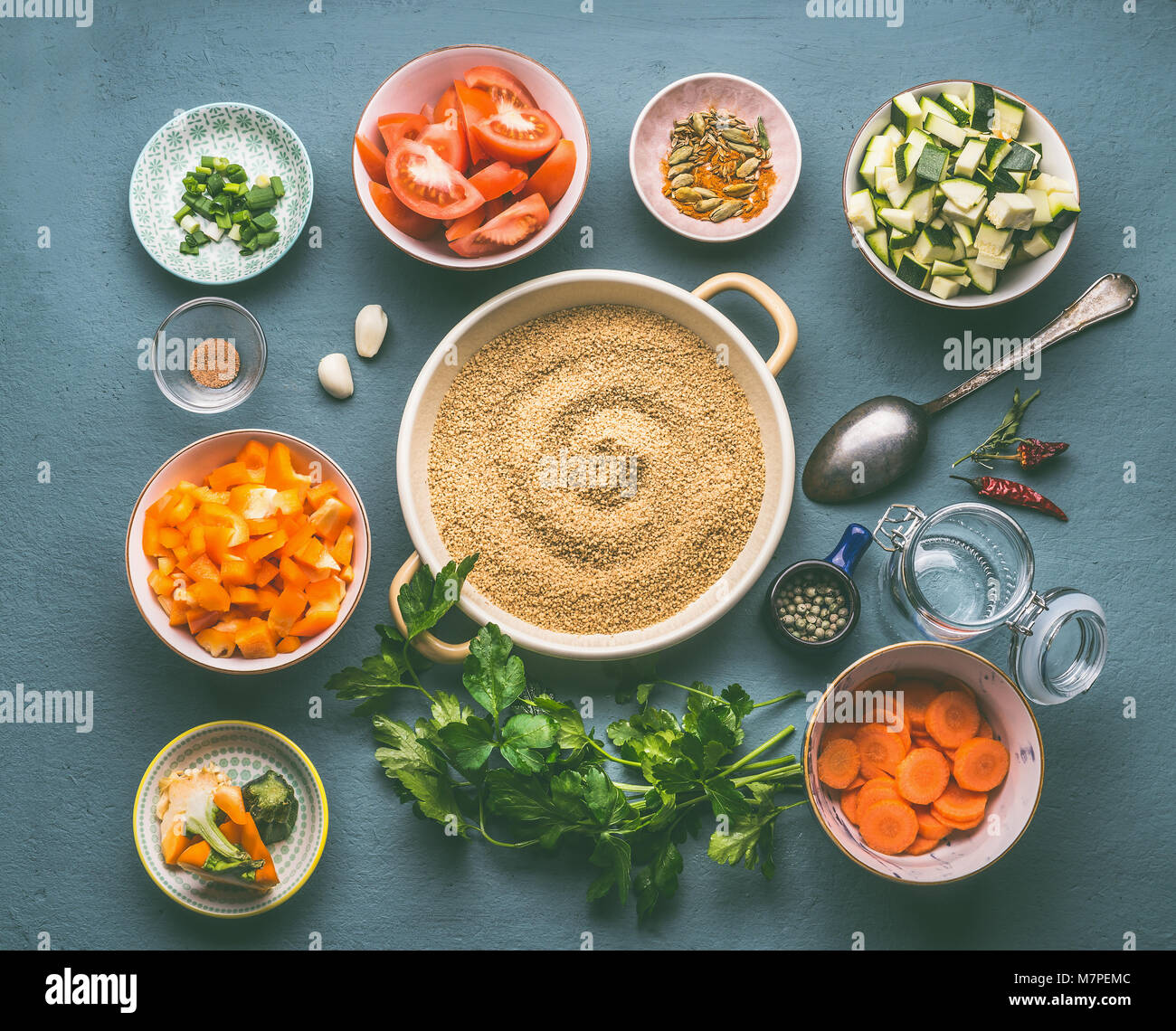 Food flat lay with couscous and vegetarian cooking ingredients in bowls on gray background, top view Stock Photo