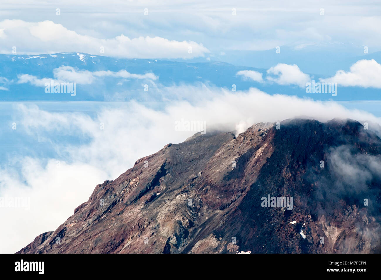 An aerial view of an Alaskan peak surrounded by smoky clouds and a blue ...