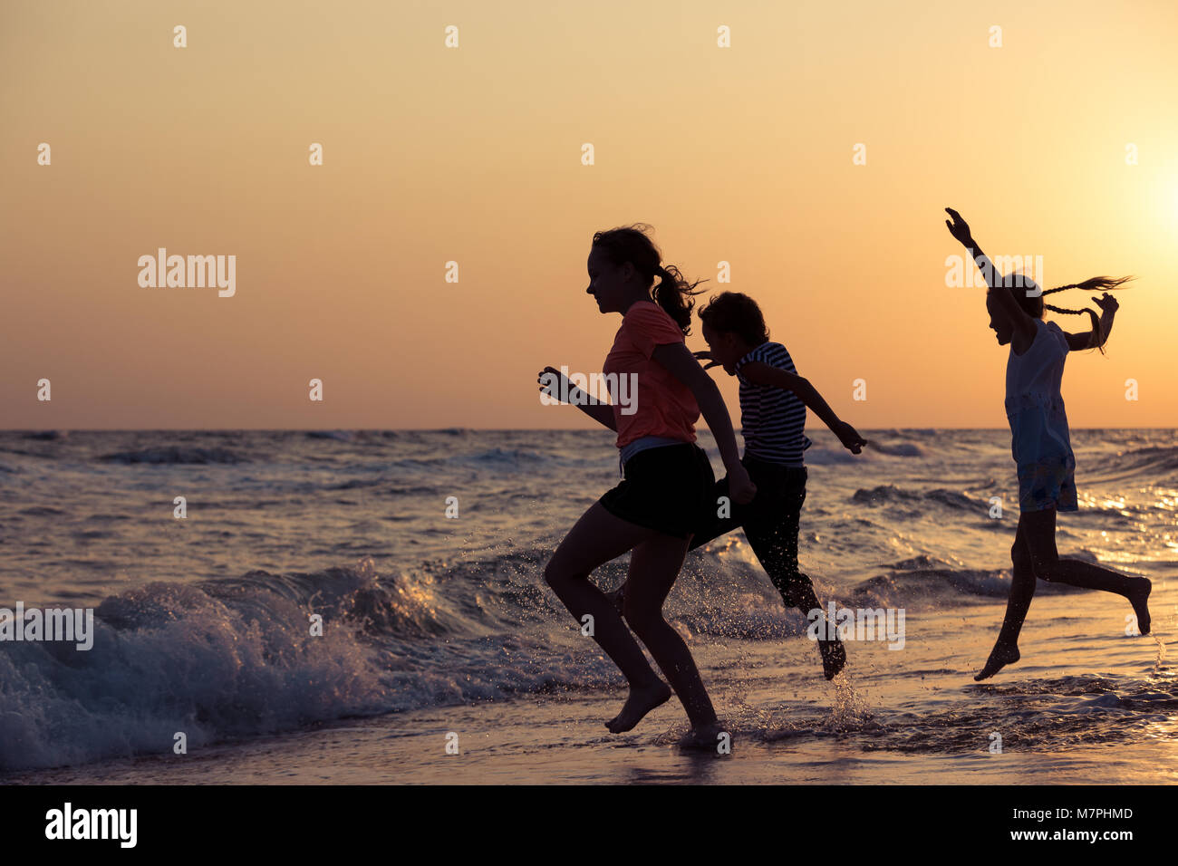 Happy children playing on the beach at the sunset time. Three Kids having fun outdoors. Concept of summer vacation and friendly family. Stock Photo