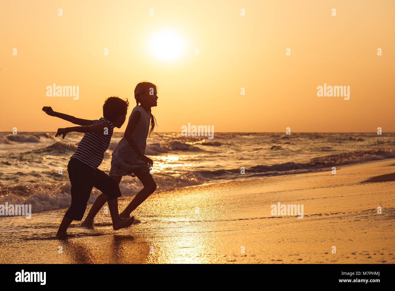 Happy children playing on the beach at the sunset time.Two Kids having fun outdoors. Concept of summer vacation and friendly family. Stock Photo