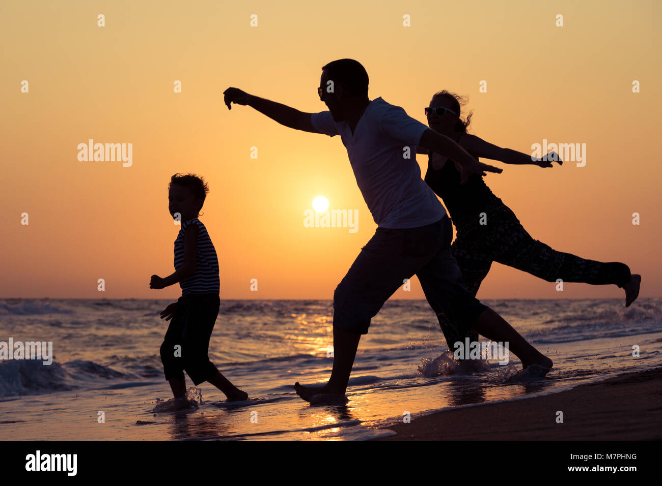 Father mother and son  playing on the beach at the sunset time. People having fun outdoors. Concept of summer vacation and friendly family. Stock Photo