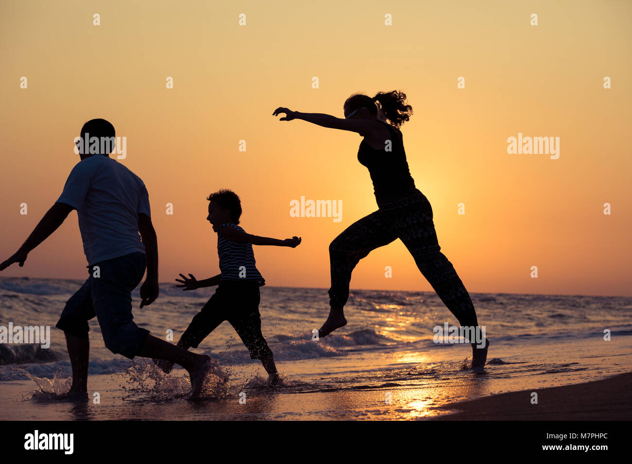 Father mother and son  playing on the beach at the sunset time. People having fun outdoors. Concept of summer vacation and friendly family. Stock Photo