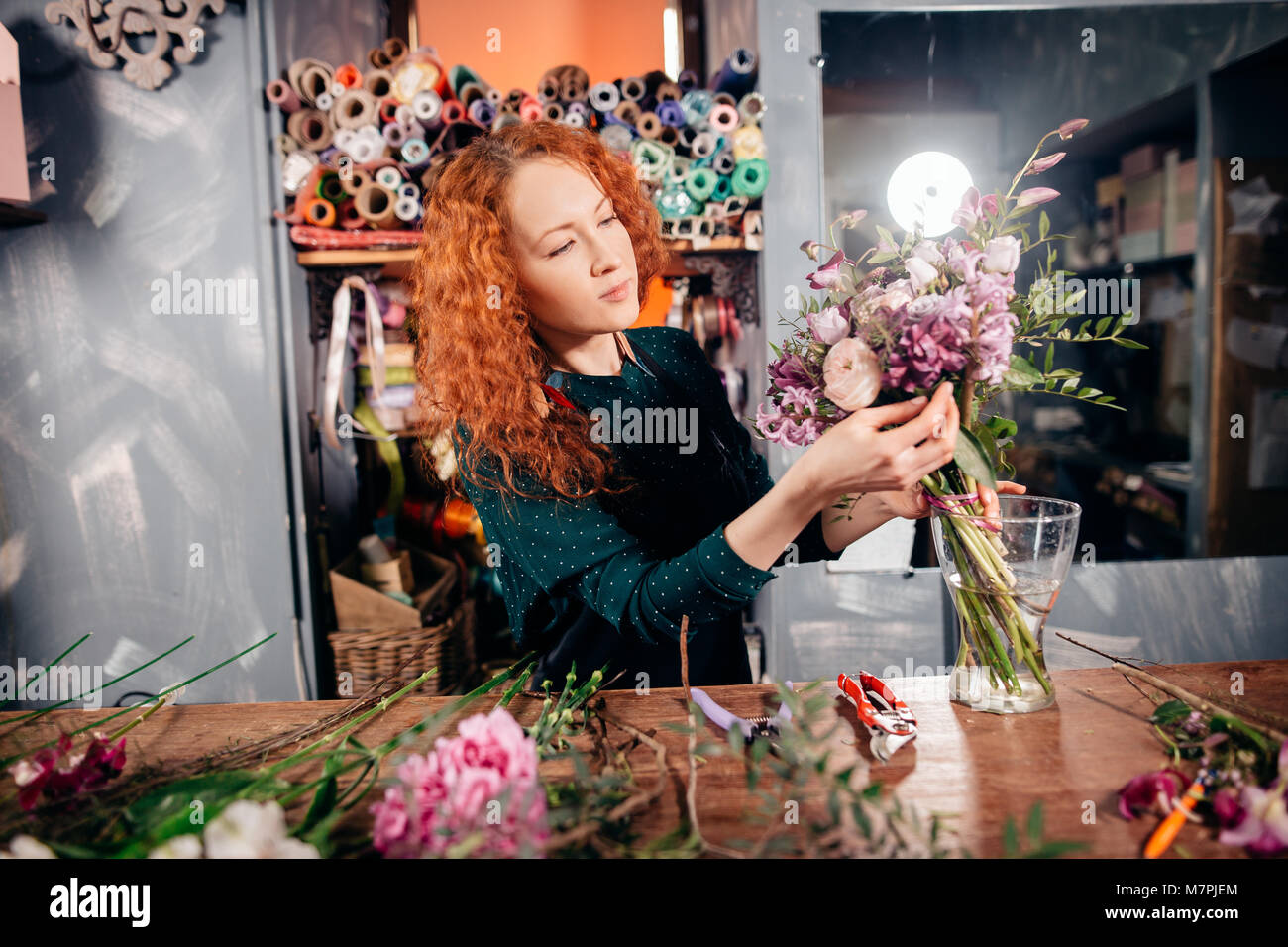 image of young Caucasian hardworking flower asistant concentrating on her work, holding a bounch of natural flowers at store Stock Photo