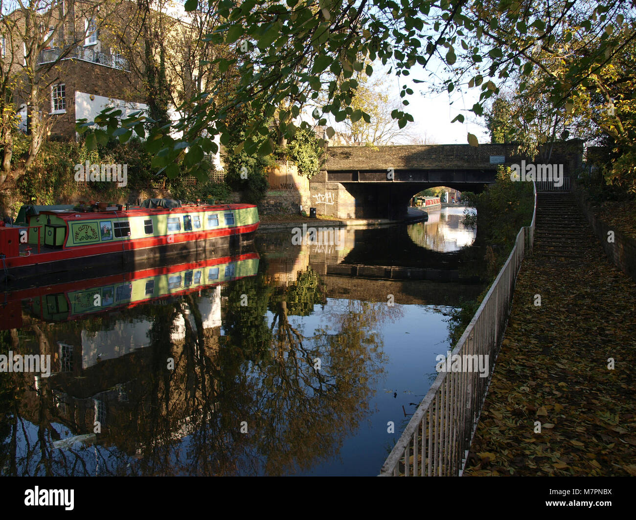 Reflections of a bridge, a barge and trees in the water of the Regents Park Canal in autumn Stock Photo