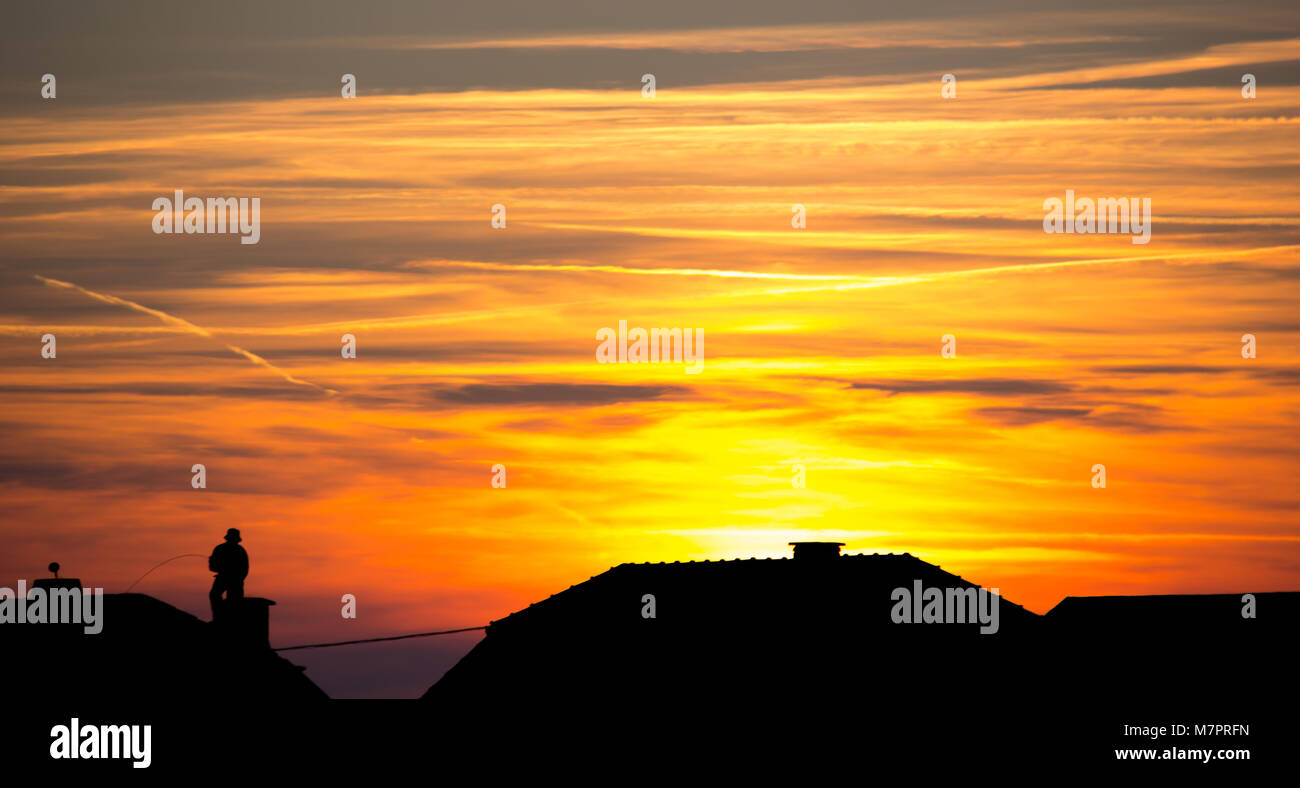 Chimney sweep at work on the rooftop - sunset and silhouette Stock Photo