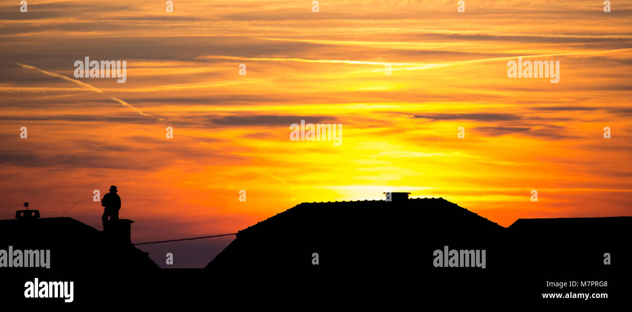 Chimney sweep at work on the rooftop - sunset and silhouette Stock Photo