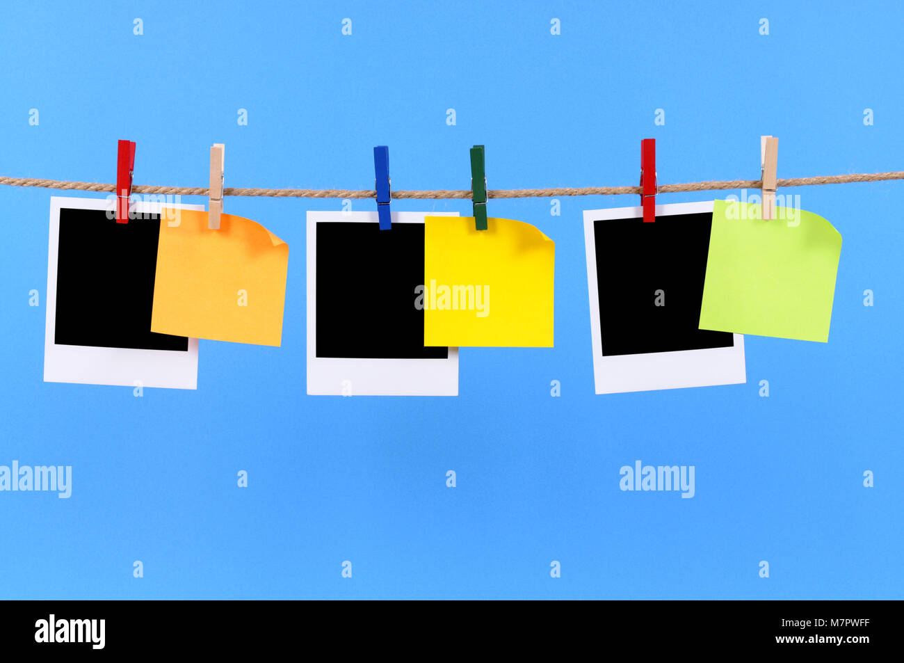 Blank instant camera photo prints and office sticky notes hanging on a rope or string isolated against a blue background.  Space for copy. Stock Photo